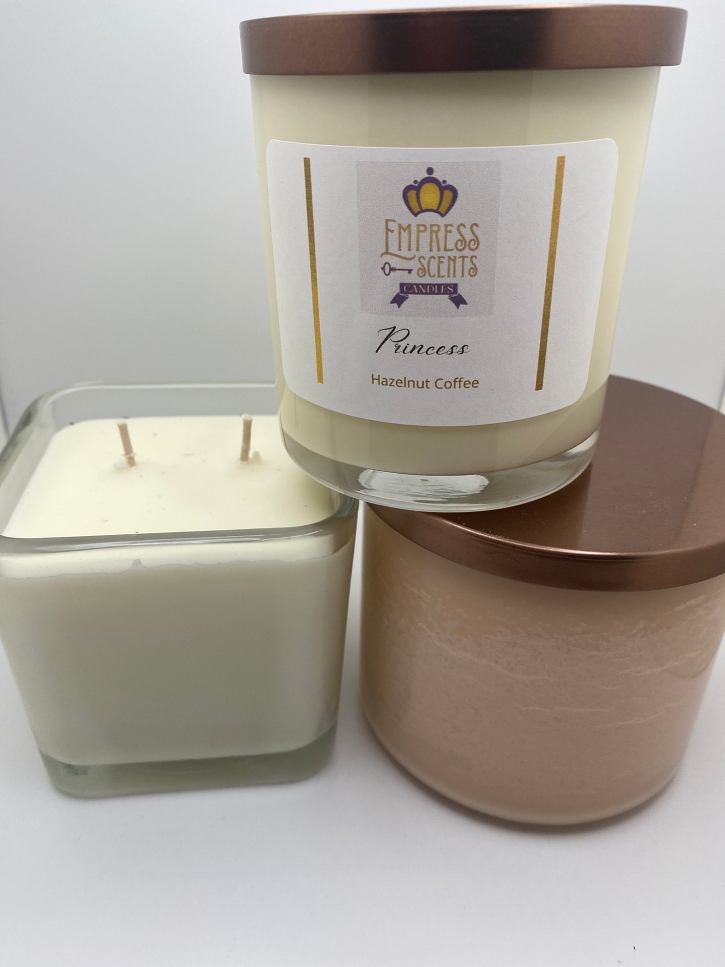 one cylindrical candle jar with white candle wax, one cylindrical candle jar with light brown candle wax, one cube-shaped jar with white candle wax